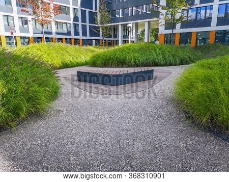 Wooden Bench With Green Bushes Around And White Corporate Buildings