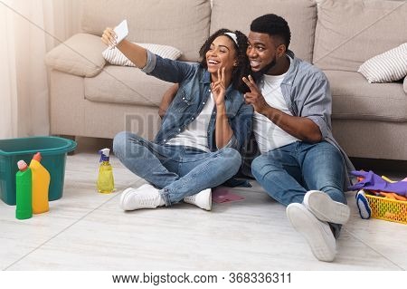 Happy Black Couple Taking Selfie On Smartphone After Tidying Flat Together, Relaxing On Floor After 