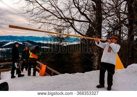 Bukovel Ski Resort. Grandfather In An Embroidered Shirt Plays The Trembita For Tourists Against The 