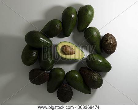 Sliced And Whole Avocado Fruits Of Different Varieties Of Green And Brown On A Light Background.