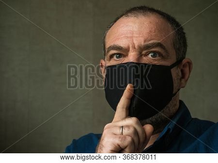 A man in a medical mask with a finger at his mouth. Coronavirus fake news and conspiracy theories concept