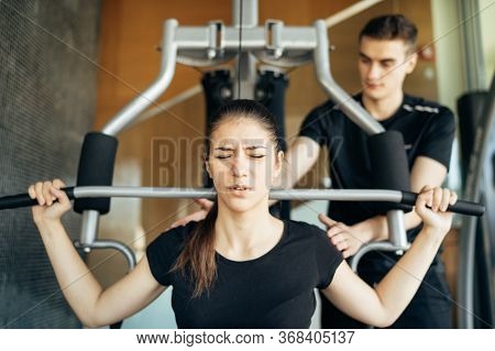 Woman Doing Fitness Exercises On Home Gym Lat Pull Down Machine With Personal Trainer.making An Effo