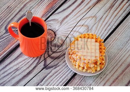 A Stack Of Fresh Waffles With Syrup And An Orange Mug With Black Coffee On A Wooden Table.