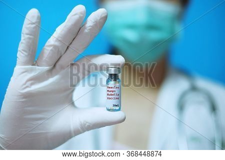 A Female Asian Physician With Surgical Mask And White Rubber Gloves At A Clinic, Holding A Glass Bot