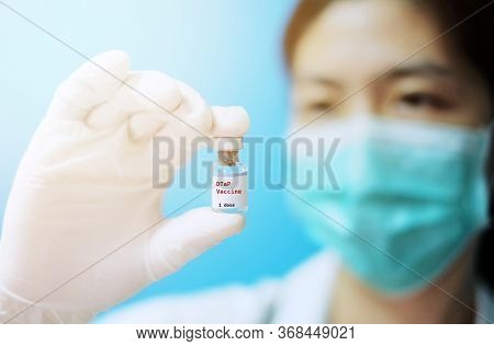 A Female Asian Physician With Surgical Mask And White Rubber Gloves At A Clinic, Holding A Glass Bot