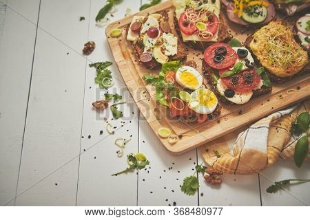 Tasty, homemade small sandwiches with various ingredients served on wooden chopping board. Vege kitchen concept. Top view.