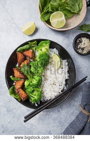 Vegan Teryaki  Tempeh Or Tempe Buddha Bowl  With Rice, Steamed Broccoli, Spinach  And Lime On Gray B