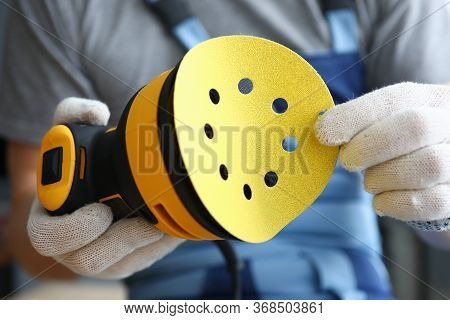 Close-up Of Professional Craftsman Changing Disc On Electrical Yellow Sander. Worker Wearing Protect