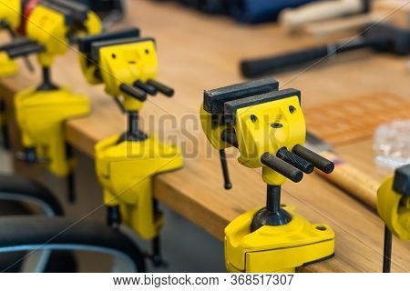 Many Yellow Vises Are Set On The Work Bench At The School. New Grips Or Jaw Vices Fixed At Woodwork 