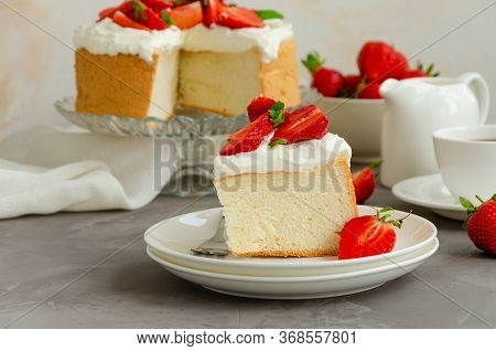 Angel Food Cake With Whipped Cream And Slices Of Fresh Strawberries On Top On A Concrete Background.