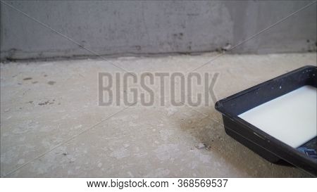 The Primer Is Poured. Wall Primer Mix. A Worker Pours A Primer From A Black Canister. The Worker Pou