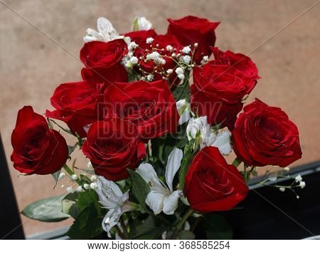 Fresh Red Roses Bouquet With Baby's Breath And White Geranium Flowers In Front Of A Sunny Glass Door