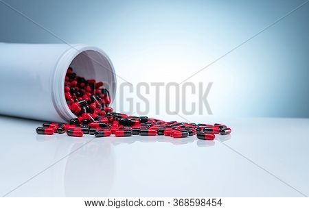 Red-black Antibiotic Capsule Pills Spread Out Of White Plastic Drug Bottle On Gradient Background. P
