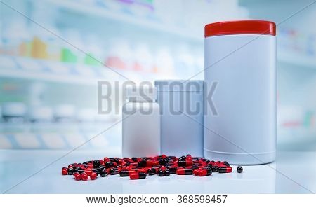 Red-black Capsules Pills Spread On Counter In Drugstore. Blank Label Plastic Drug Bottle On Blurred 