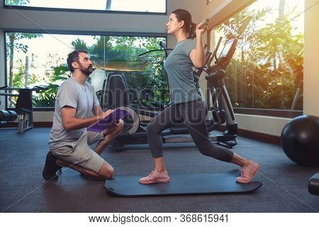 Personal Trainer Working With Client In Gym. Trainer Man Helping Young Woman With Butt Dumbbell Work