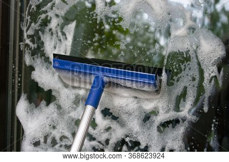 Cleaning Glass Of Window Using A Squilgee With Soap Foam. Housekeeping Concept.