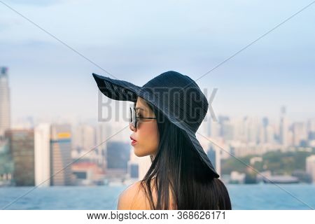 Young woman in a roof top swimming pool, infinity pool with beautiful city view. Vacation in Singapore.