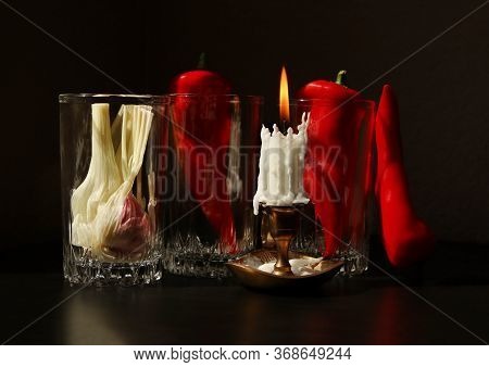 Still Life With Candlestick With Burning Candle, Red Ramiro Peppers And Garlic Bulb In The Glass Bea