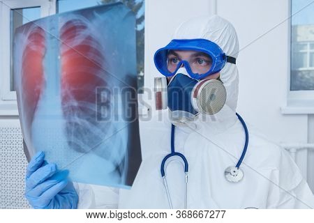 COVID-19 or 2019-nCoV. Portrait of a doctor in a protective PPE suit showing an x-ray picture of the lungs of a patient with coronavirus pneumonia. 