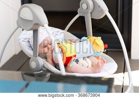 Close Up Of Little 6 Months Old Sweet Baby Girl In Electric Swing Or Cradle Outdoors On Sunny Summer