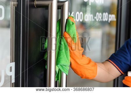 Woman Hand In Protective Orange Rubber Gloves Holding Green Microfiber Cleaning Cloth And Wiping Dus