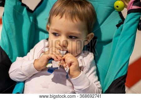 Little Cute Hungry Toddler Girl Sitting In A Stroller And Eating A Lozenge Candy Bar. Close-up, Soft