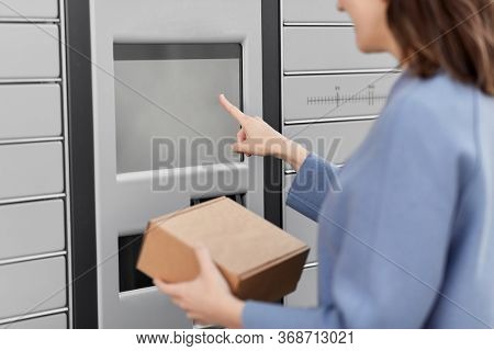 mail delivery and post service concept - close up of happy smiling woman with box at outdoor automated parcel machine choosing operation on touch screen