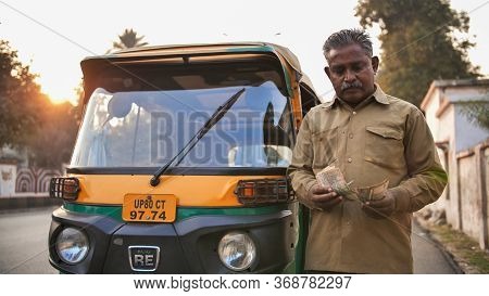 Agra, India - December 12, 2018: Indian Auto Rickshaw Tut-tuk Driver Man Recounts Money.