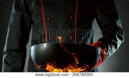 Closeup of chef holding empty wok pan in fire, ready to prepare for cooking.