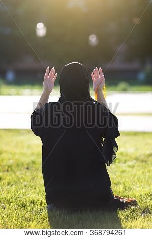 Islamic Woman Prayer In A City Park. Islamic Woman Performs Morning Prayer Sitting On Green Grass In