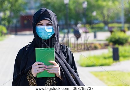 Muslim Woman Stands With A Quran In Her Hands. An Islamic Woman In National Women's Clothing Holds A