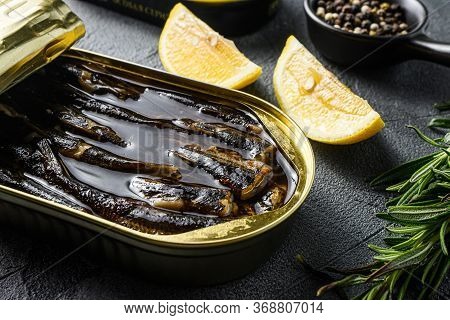 Top View Of Opened Cans With Sprats On Grey Textured Stone Table, With Herbs Rosemary, Lemon And Pep