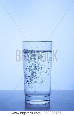 Fresh Clean Water Is Poured From A Bottle Into A Glass Cup. Light Background.