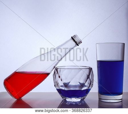 Composition From A Bottle And Glasses With Multicolored Liquid On A White Background. The Bottle Res