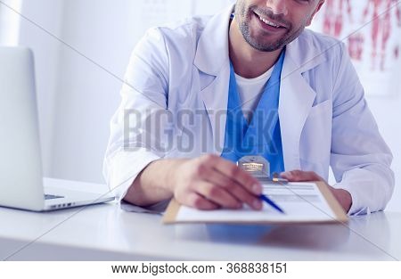 Male Doctor Using A Laptop, Sitting At His Desk