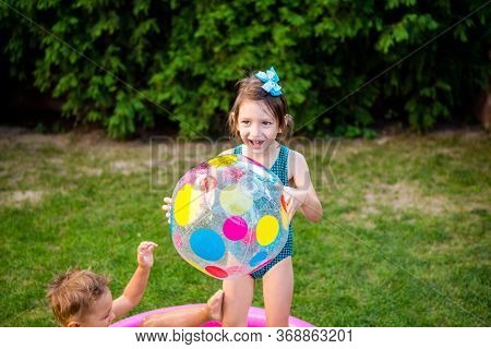 Two Children With Beach Ball At Swimming Pool. Joyful Kid Playing In Inflatable Pool Backyard. Littl