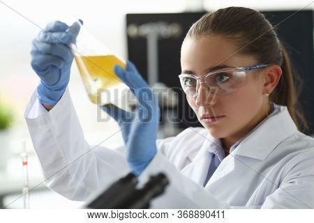 Chemist Girl Looks At Flask With Yellow Liquid. Experiments And Research Pharmacist. Laboratory Stud