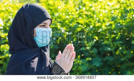 Islamic Woman In Protective Medical Mask Prays To God. Muslim Woman In A Medical Mask Prays On The S
