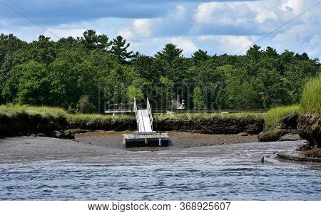 Dock Resting On A Muddy Beach Along On A River.