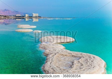 Israel. Azure sea water is full of healing salts. Small islets and path of salt in the water. Early morning at the resorts of the Dead Sea. Concept of ecological, medical and photo tourism