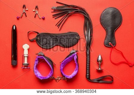 Bdsm Kit From Sex Shop. Leather Whip, Buttplug, Vibrator, Dildo, Nipple Clamps And Other On Red Back