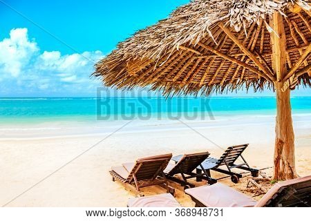 A Sun Lounger Under An Umbrella On The Sandy Beach By The Ocean And Cloudy Sky. Vacation Background.