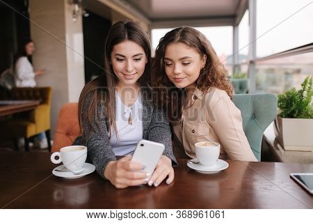 Two Girls Friend Drink Coffee In Cafe And Look In Smat Phone. Happy Smiled Women Sittng On Terrace. 