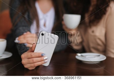 Two Girls Friend Drink Coffee In Cafe And Look In Smat Phone. Happy Smiled Women Sittng On Terrace. 