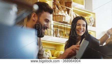Close Up Of Caucasian Young Male And Female Bread Vendors Selling Baguettes To The Buyer At The Coun