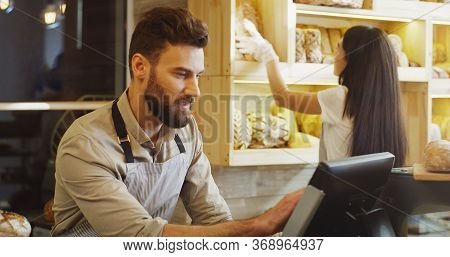Close Up Of Caucasian Young Male And Female Bread Vendors Selling Baguettes To The Buyer At The Coun