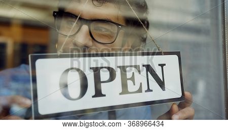 Close Up Of The Male Caucasian Hands Turning A Signboard On The Glass Door Of The Shop From Closed T