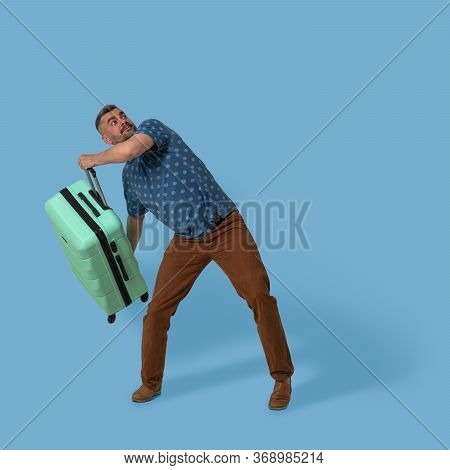 Man Holds Plastic Suitcase Posing In Studio On Blue Background. Caucasian Man Going To Throw His Gre