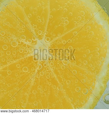 Fresh Lemon Slice In Liquid With Bubbles. Close-up Of A Lemon Slice In Soda Water. Bubbles On Lemon.