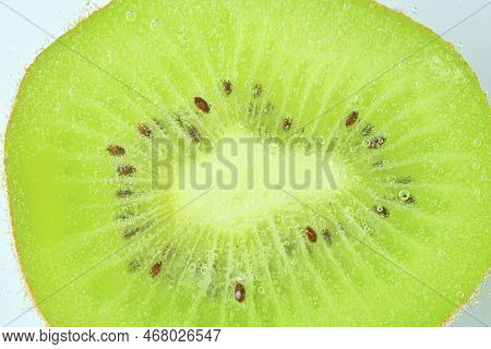 Close-up Of Kiwi Fruit In Liquid With Bubbles. Slice Of Green Ripe Kiwi Fruit In Sparkling Water. Ju